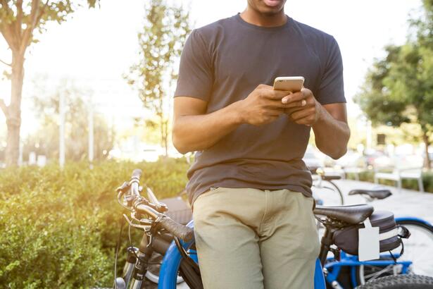 man leaning against a bicycle and holding a mobile phone in front of him
